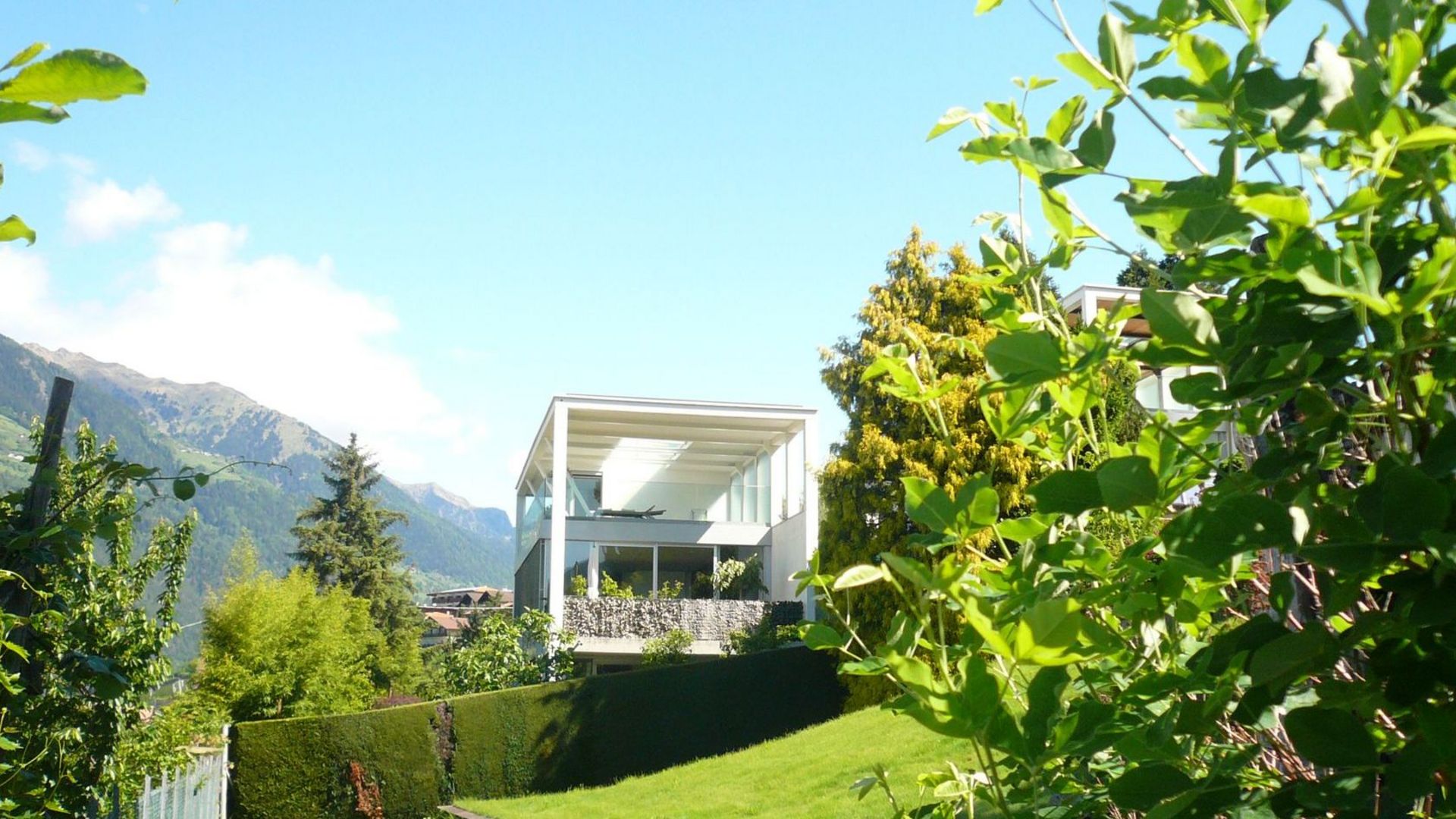 Modernes weißes Haus mit Terrasse, grüner Garten und Berglandschaft im Hintergrund. Modernes weißes Haus mit Terrasse, grüner Garten und Berglandschaft im Hintergrund.