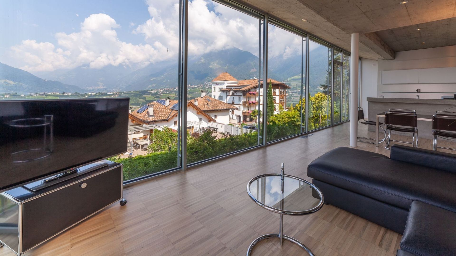 Modernes Wohnzimmer mit bodentiefen Fenstern und Panoramablick auf Dächer und Berge. Modernes Wohnzimmer mit bodentiefen Fenstern und Panoramablick auf Dächer und Berge.