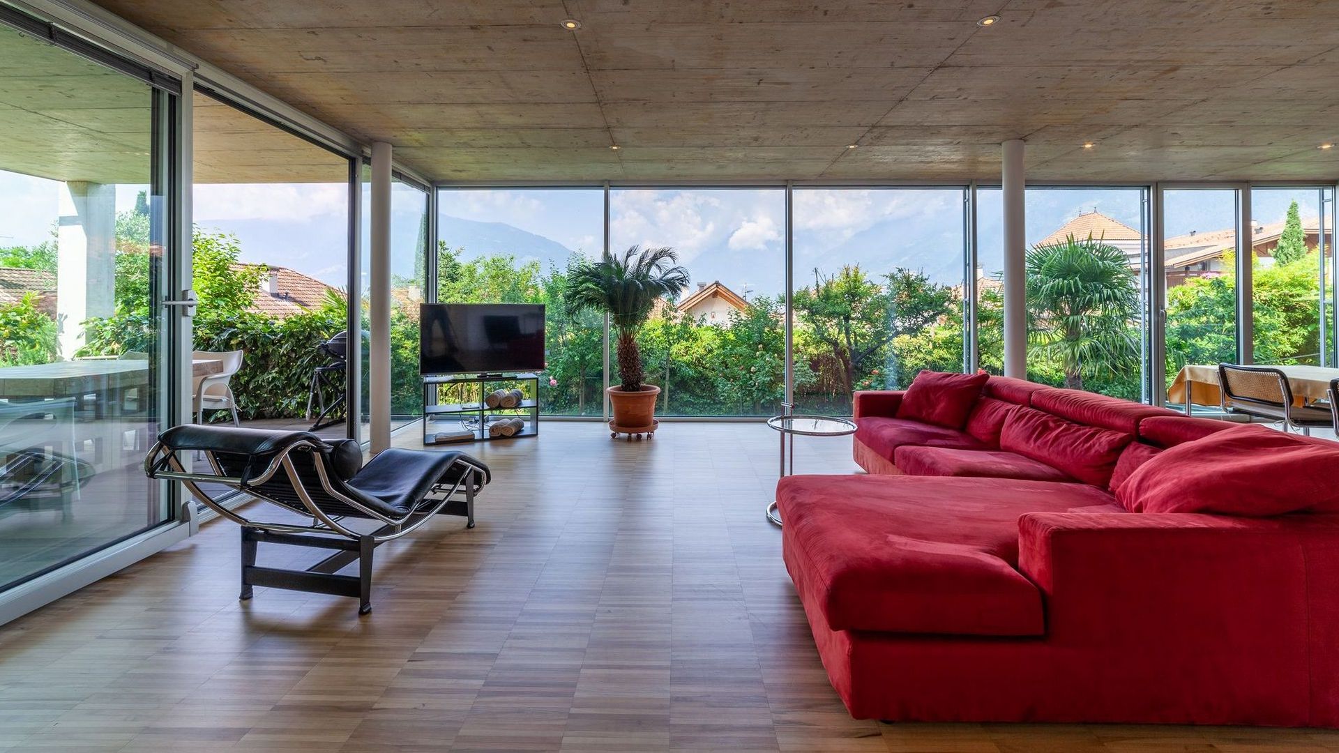 Helles Wohnzimmer mit großen Glasfenstern, rotem Ecksofa und Palmenblick. Helles Wohnzimmer mit großen Glasfenstern, rotem Ecksofa und Palmenblick.