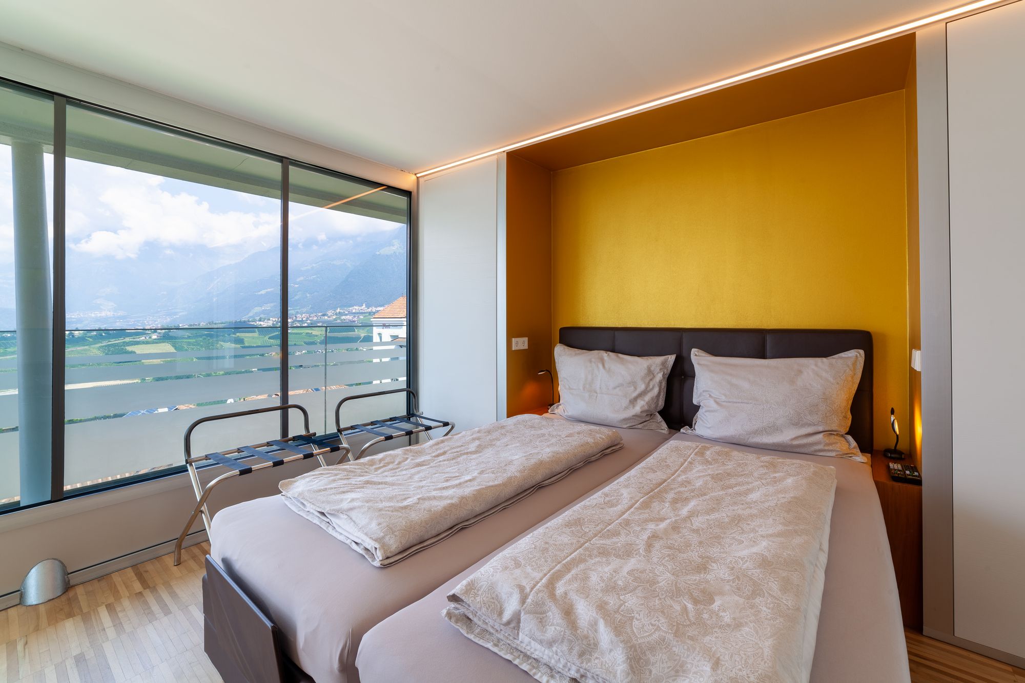 Schlafzimmer mit zwei Betten, gelber Akzentwand und großer Fensterfront mit Bergblick Schlafzimmer mit zwei Betten, gelber Akzentwand und großer Fensterfront mit Bergblick