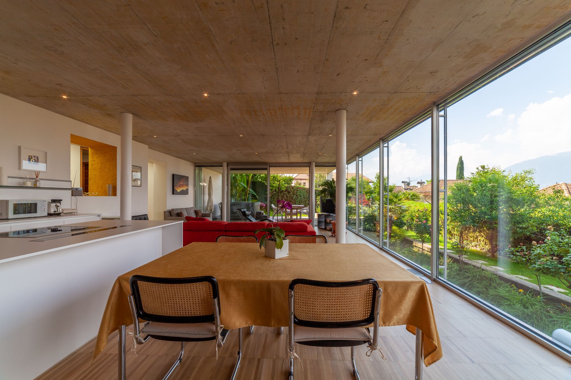 Helles, modernes Wohn- und Esszimmer mit Esstisch, roter Couch und bodentiefen Fenstern zum Garten Helles, modernes Wohn- und Esszimmer mit Esstisch, roter Couch und bodentiefen Fenstern zum Garten