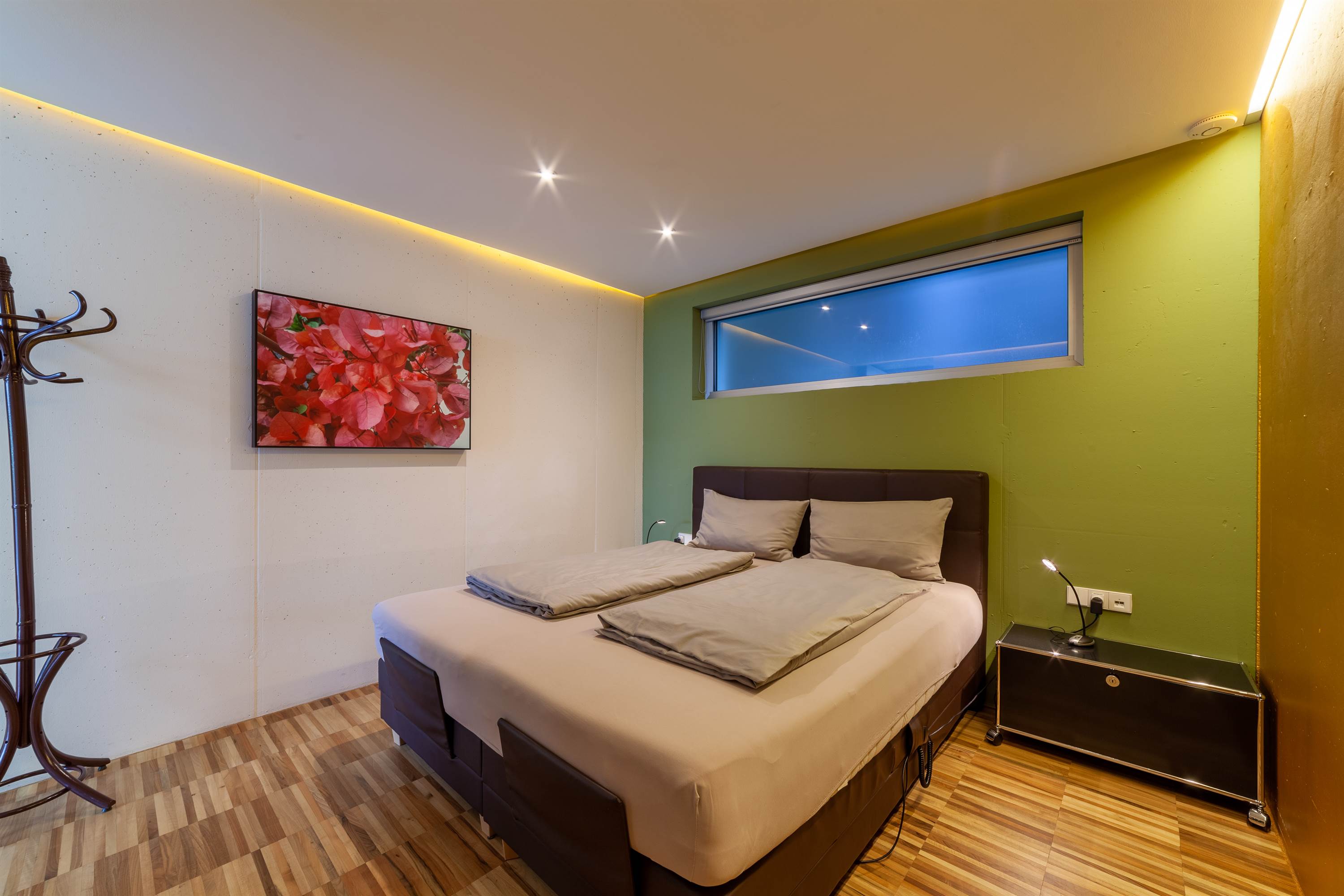 Modernes Schlafzimmer mit Doppelbett, grüner Wand, schmalem Fenster und einem Bild mit roten Blumen Modernes Schlafzimmer mit Doppelbett, grüner Wand, schmalem Fenster und einem Bild mit roten Blumen