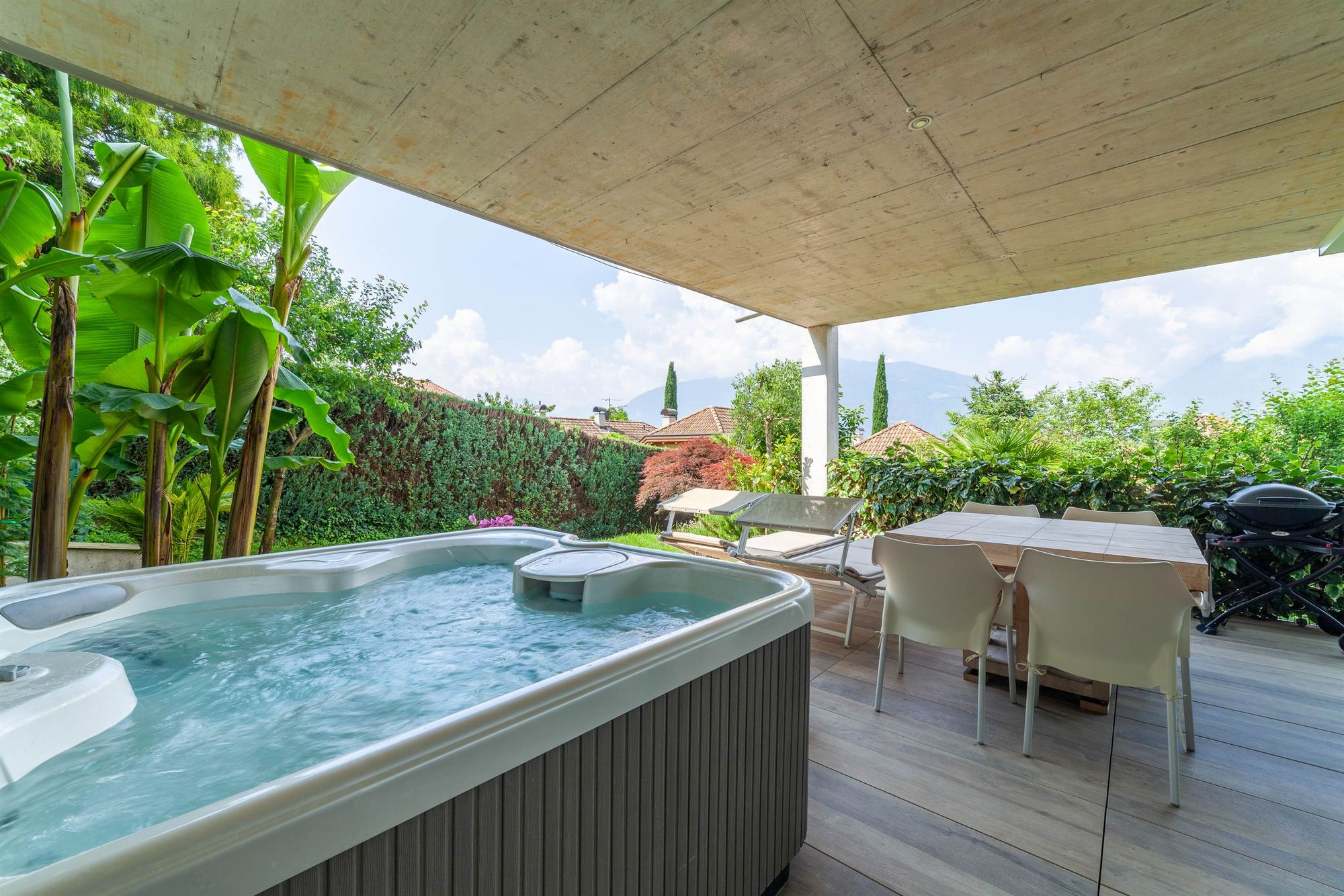 Überdachte Terrasse mit Whirlpool, Esstisch, Liegen und Blick auf Garten und Berge Überdachte Terrasse mit Whirlpool, Esstisch, Liegen und Blick auf Garten und Berge
